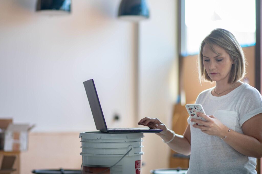 Woman looking at cell phone to enter info into a laptop